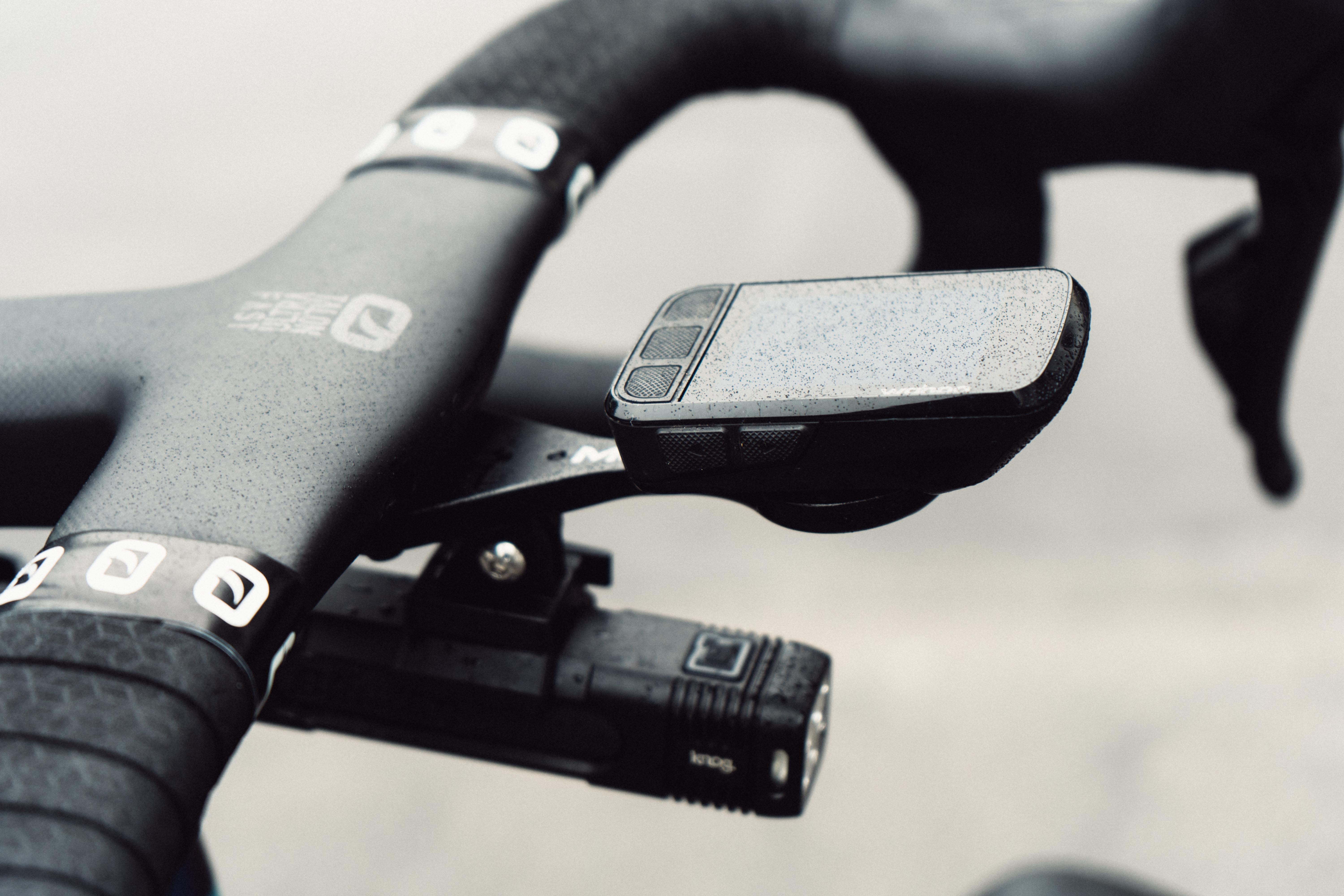 A close up of the cockpit of a bike, with bike computer and headlight attached