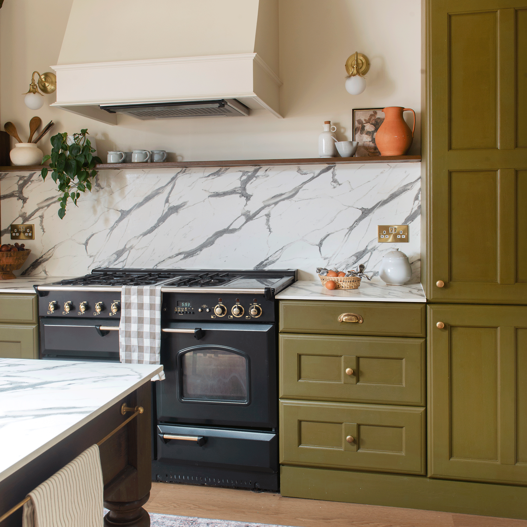 a green kitchen with a marble countertop and splashback and a black range cooker
