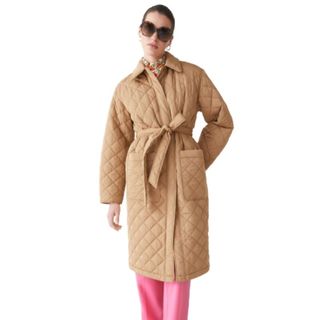 model wearing belted quilted beige coat with pink trousers and sunglasses