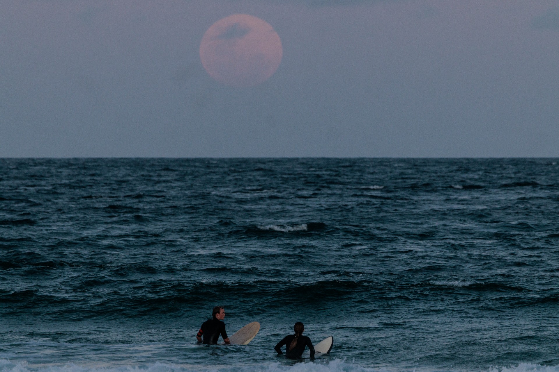 At Manly Beach in Sydney, surfers take to the waves beneath the large red moon's face. (Photo by Brook Mitchell via Getty Images)