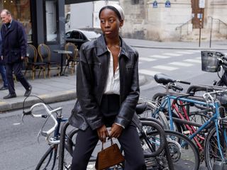 French fashion influencer Syvlie Mus is Paris wearing an on-trend fall look including a vintage leather jacket, head scarf, white shirt, black pants, strappy heels, and a mock croc bag.