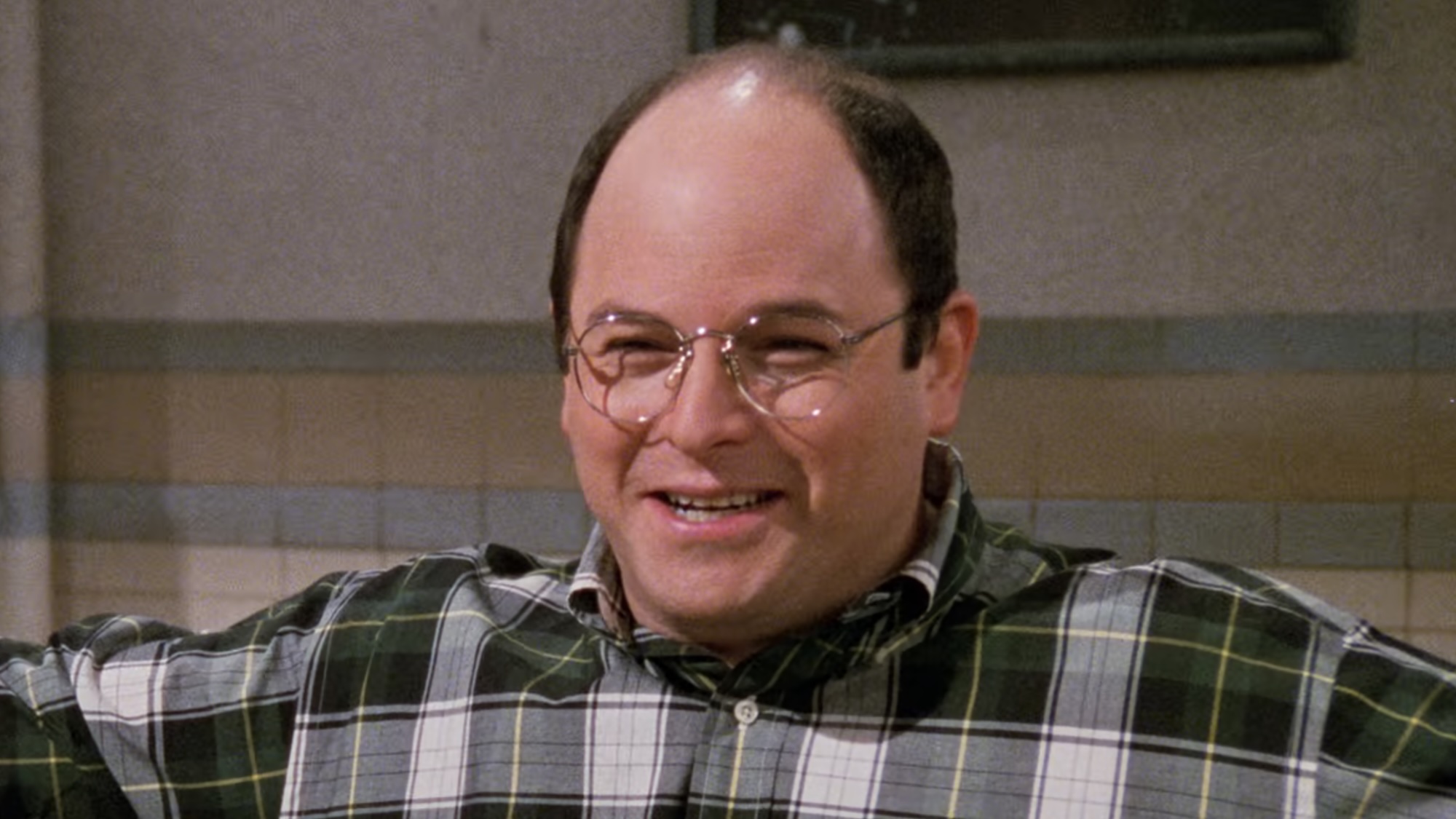George smiling at Jerry and Elaine while sitting in Monk's Diner in Seinfeld