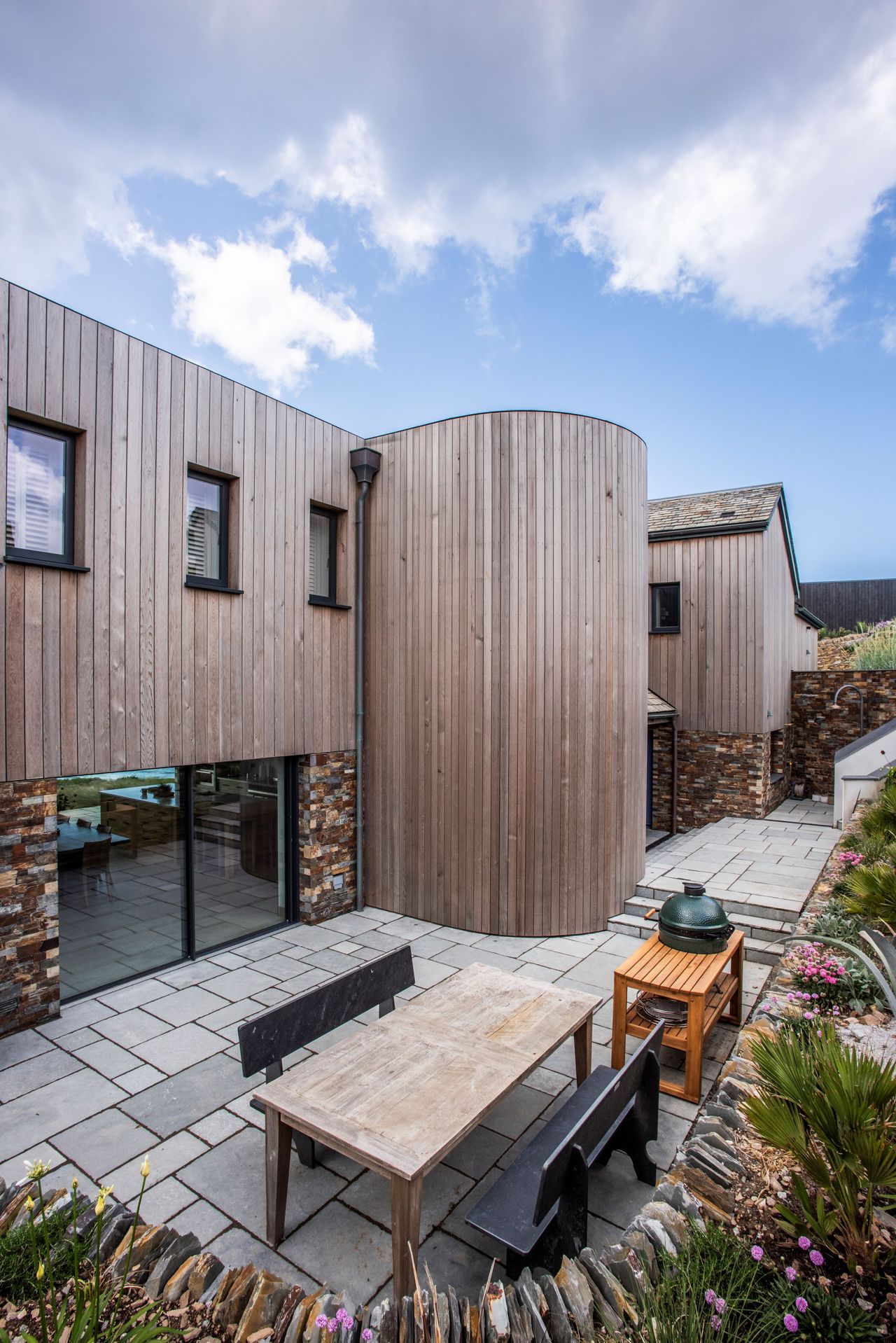 The side of the house shows wooden panelled walls and an outdoor BBQ area