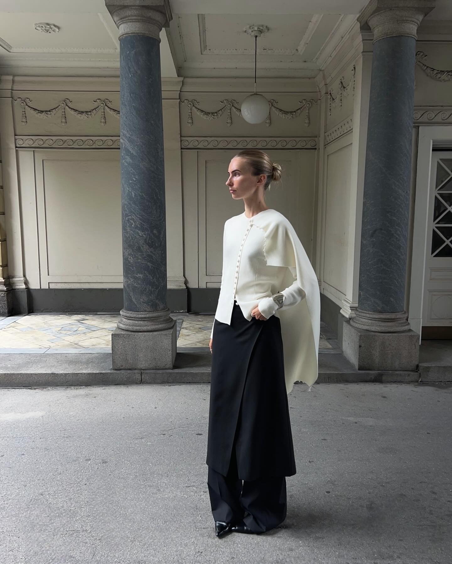 Woman wears cream cardigan with scarf attachment, black skirt and black trousers