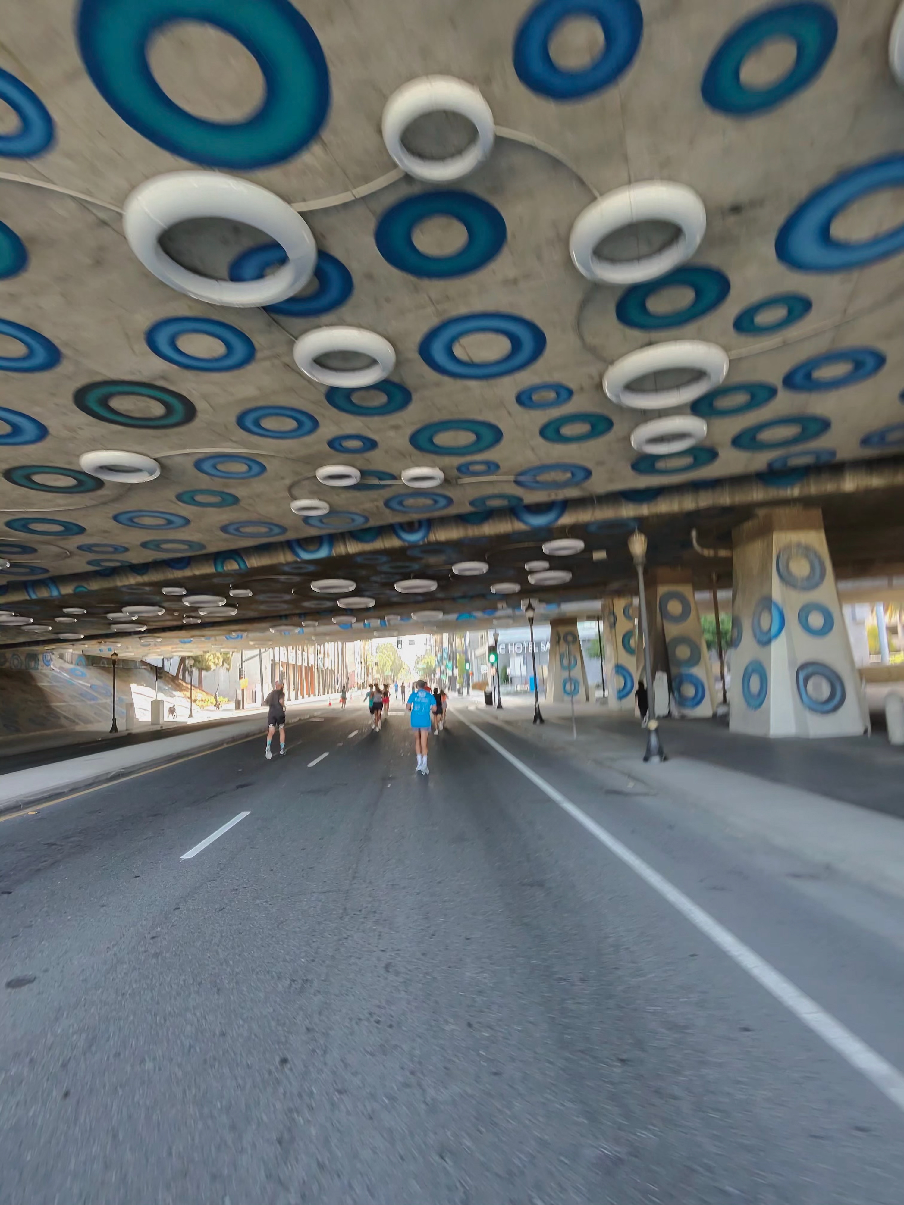 A Ray-Ban Meta smart glasses camera sample at the San Jose Half Marathon showing an underpass with artistic blue and white circles and runners underneath it.