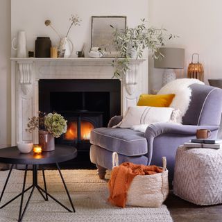 Armchair and coffee table pulled up in front of a marble fireplace with fire burning and lots of natural materials on display