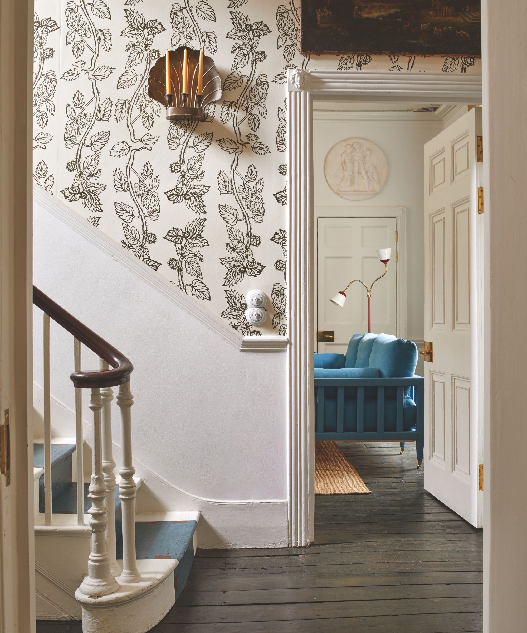 A staircase with a blue runner and walls covered in a nettle print wallpaper