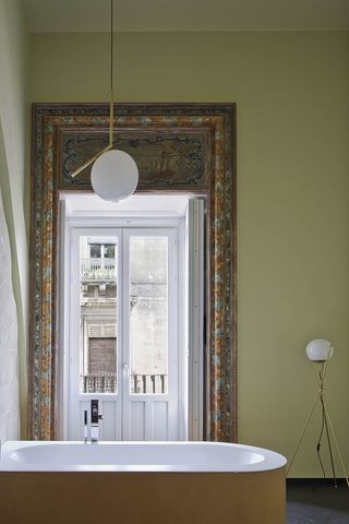 A beige bathroom with a white tub, a round floor lamp and a large door with a decorated frame.
