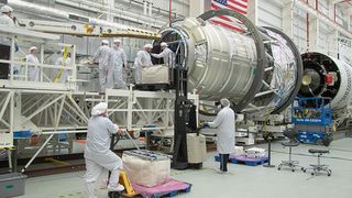 Scientists are seen in their clean room clothes with a giant metal cylinder representing the new experiment.
