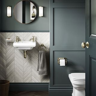 An under stairs toilet with dark grey panelling and herringbone tiles