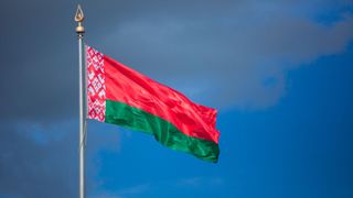 A Belarusian flag flying against a blue sky with some dark clouds