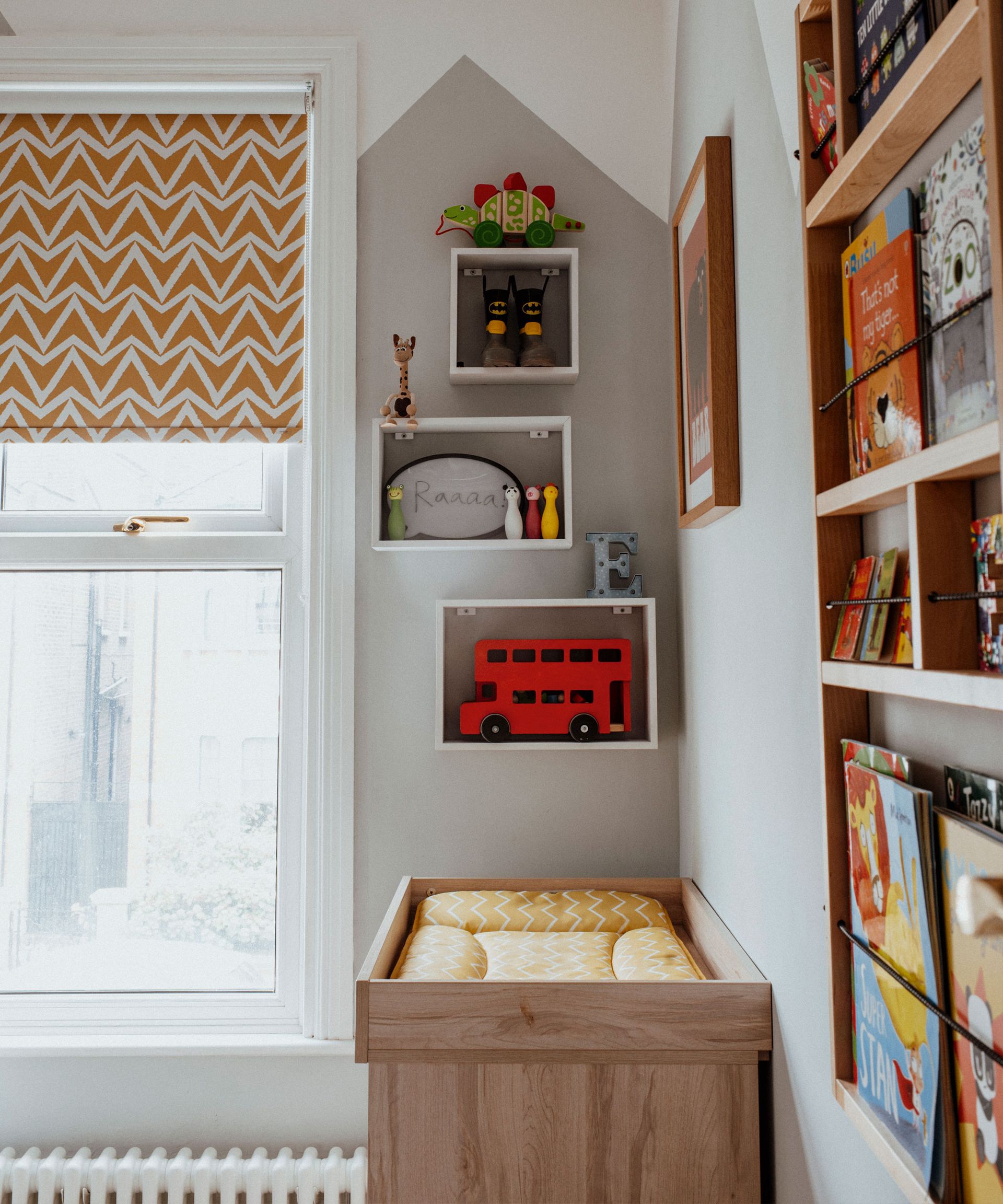 Painted kids bedroom with grey abstract design, wall mounted wooden shelves with toys and decorative items, wall mounted wooden book shelf, yellow patterned blind, white painted crib
