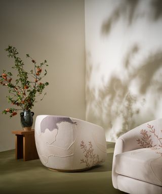 A white room with green floors, two embroidered armchairs and a wooden side table