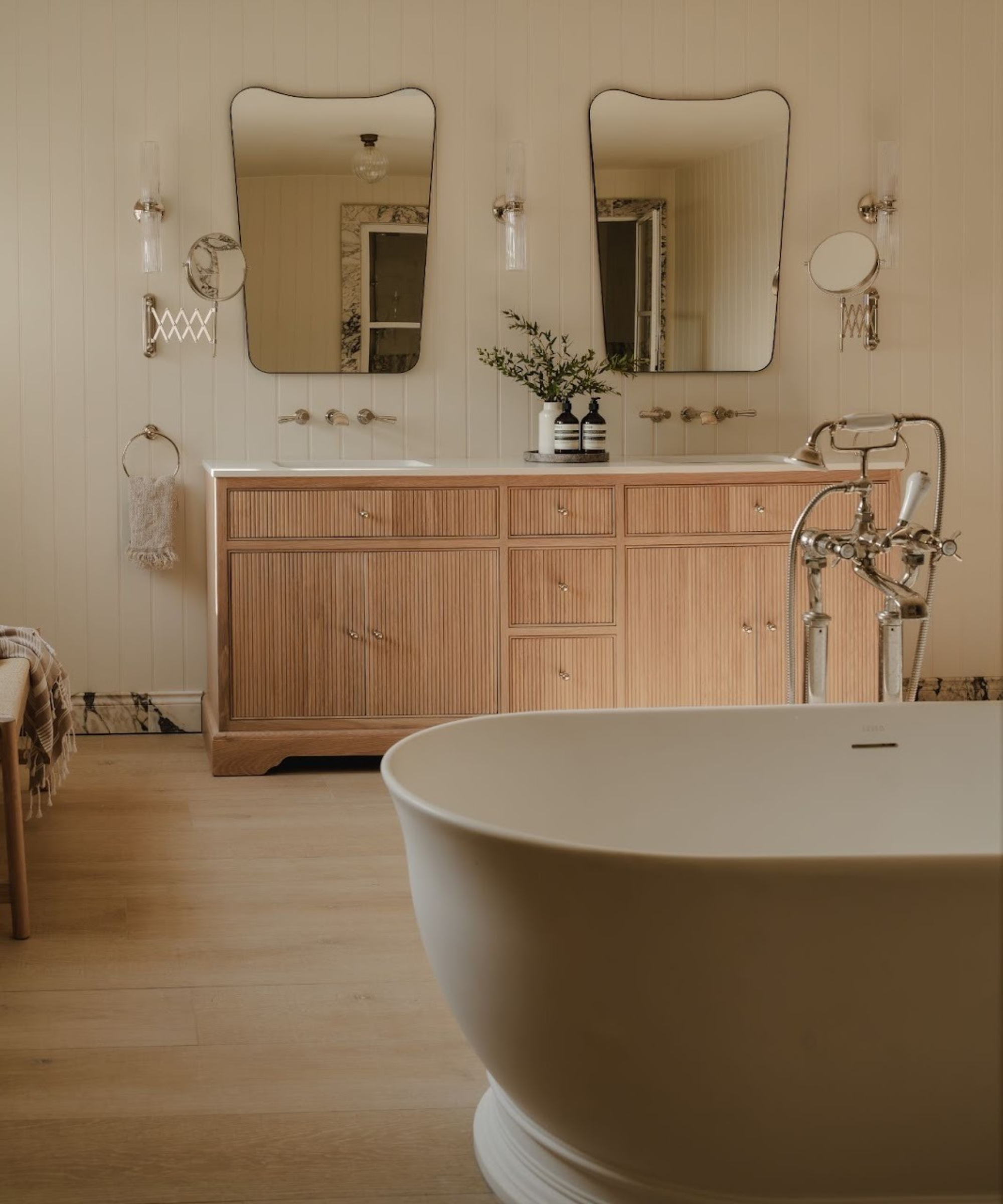 bathroom with wooden double vanity unit with mirrors above and freestanding bath