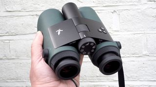 Swarovski Optik AX Visio binoculars held in a hand in front of a white wall
