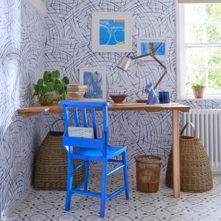 home office with blue wallpaper and blue floor, desk, blue painted chair, artwork, baskets, books