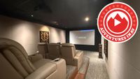 A home theatre reference room with leather recliners, a ceiling mounted projector, and a projector screen