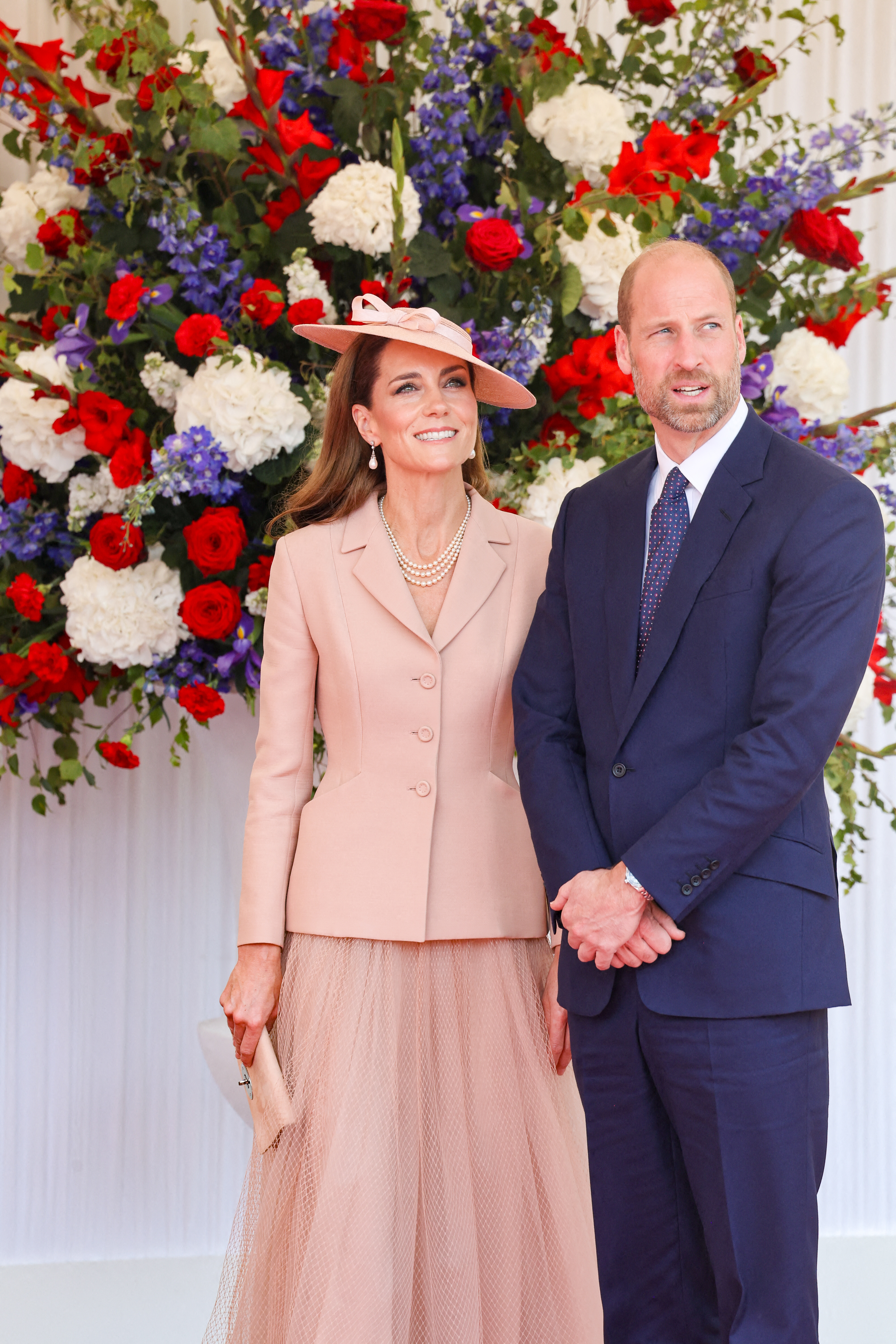 Kate Middleton in a pink jacket and skirt standing next to Prince William