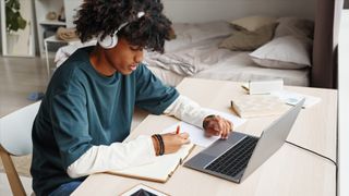 Portrait of African-American teenage boy studying at home or in college dorm and using laptop, copy space