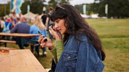 best waterproof eyeliner - girl in denim jacket applying eyeliner at a festival