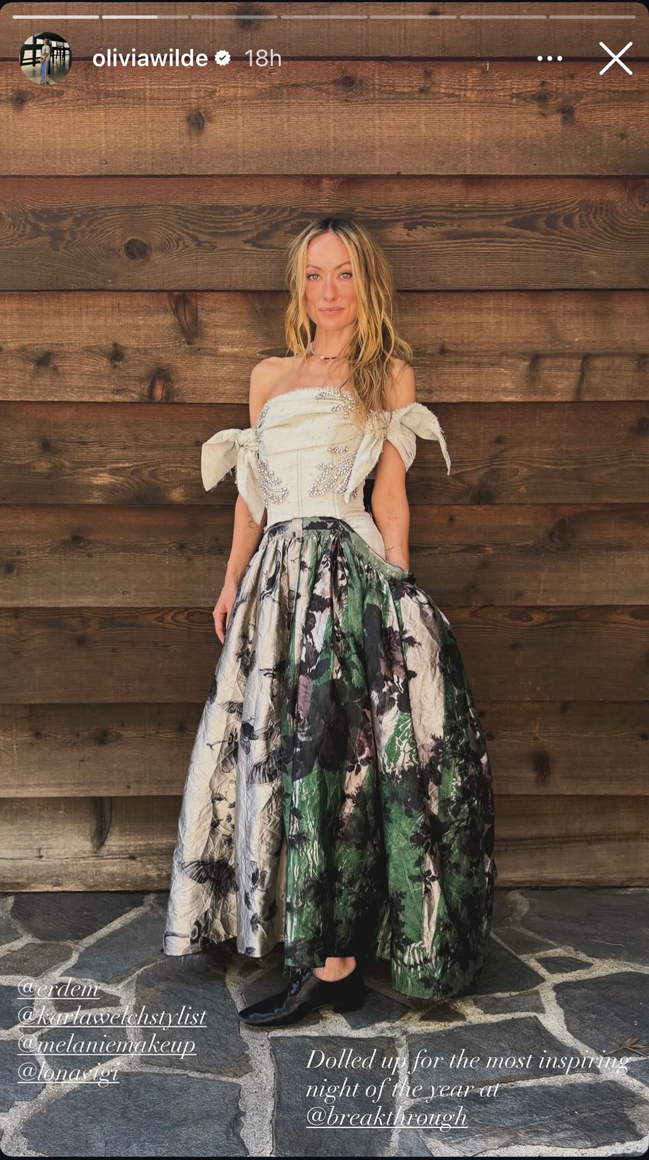 Olivia Wilde in a bodice core dress and black flat shoes heading to a Santa Monica event. She is standing in front of a wooden wall.