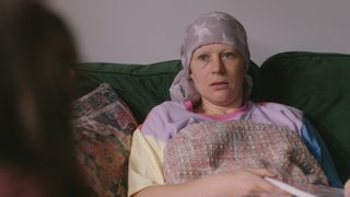 Lucy Lowe as Rachel, in a lilac headscarf with white stars on it under a blanket and talking to Jodie.