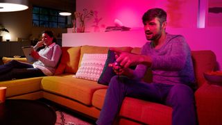 Two people on couch illuminated with white and pink Philips Hue lights