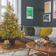 dark painted living room with a grey sofa and a wooden coffee table, with a christmas tree 