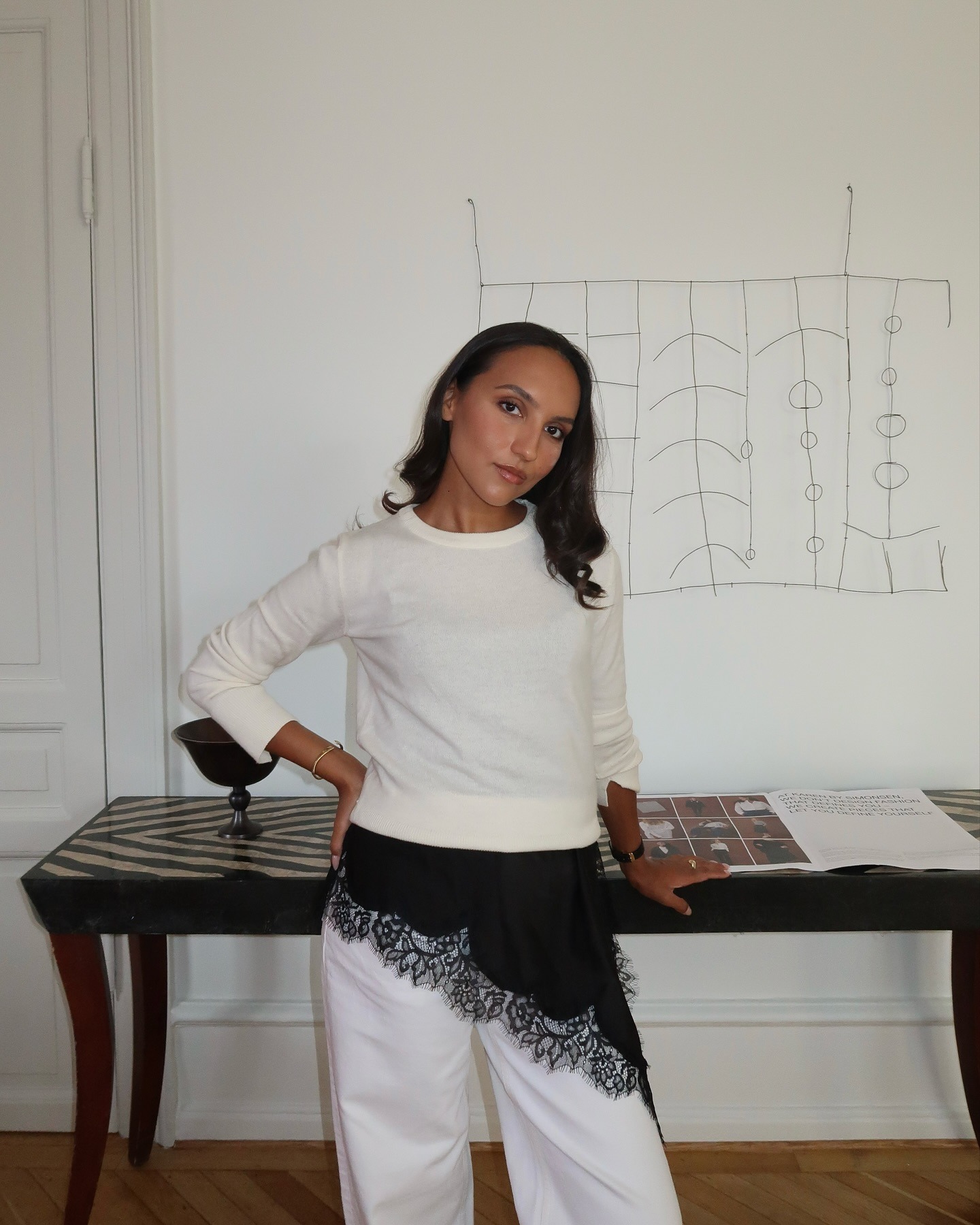 Woman in a white sweater, a black lace-trim top, and white jeans.