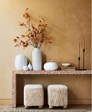 An entryway side table with white pumpkins and two taper candles