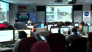 Science team members gather in the command center on Earth to manage Curiosity on Mars.