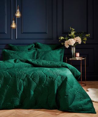 A black bedroom with double bed covered in luxury forest green bedding