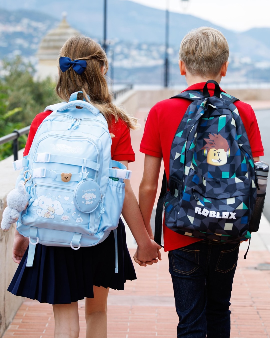 Prince Jacques and Princess Gabriella turning away from the camera to show blue backpacks and holding hands