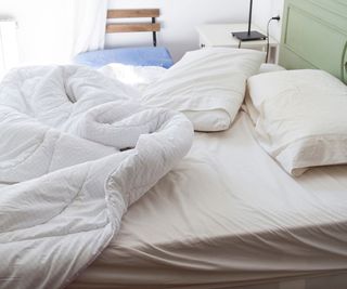 A mattress on a bed with rumpled white bedding against a white wall.