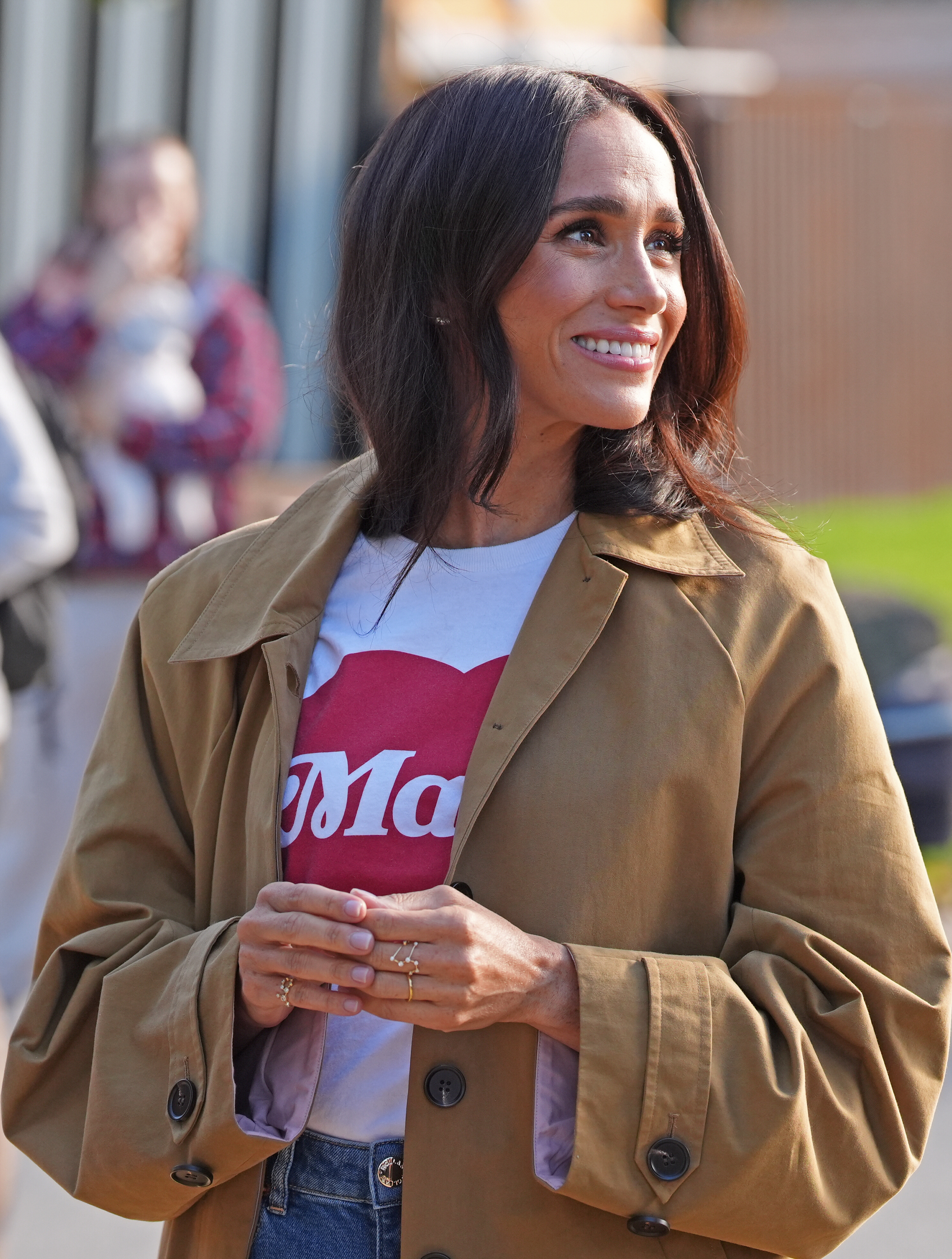 Meghan Markle smiling in a trench coat and graphic tee