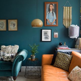 A teal-painted living room with a matching velvet sofa and an orange leather sofa