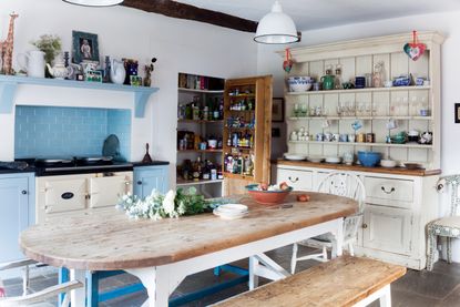 freestanding kitchen in a restored Georgian farmhouse, with a white dresser to the right, a large wooden dining table, a white aga within a blue tiled installed unit, and a wooden larder built into the wall 