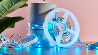 The LED light strip is lit up light blue and has been coiled around a two-tone cement cylinder. The light reel is leaning on the cylinder, and the light's control box is placed to the left.