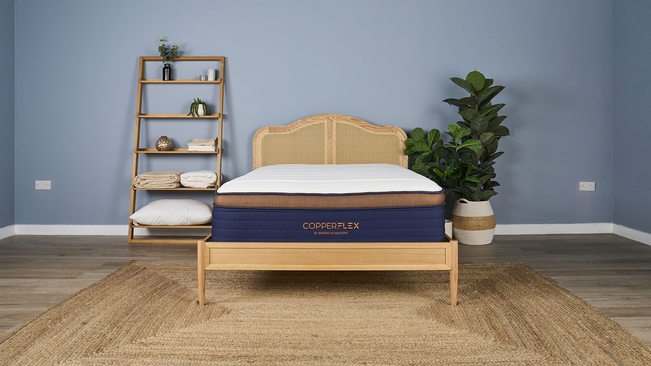 White, navy and bronze Brooklyn Bedding CopperFlex Pro Hybrid Mattress on rattan bedframe in sleep studio with shelves and plants