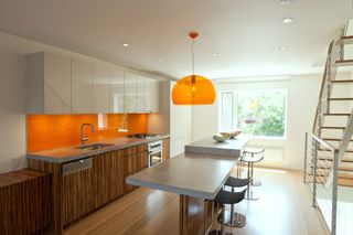 A kitchen with a bright orange gloss backsplash and an orange pendant light fixture
