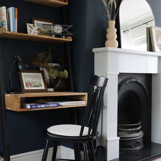 Living room with navy walls, white fireplace and desk attached to the wall.
