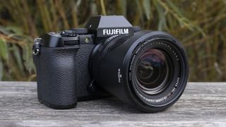 Kameraet Fujifilm X-S10 på en benk med vegetasjon i bakgrunnen.