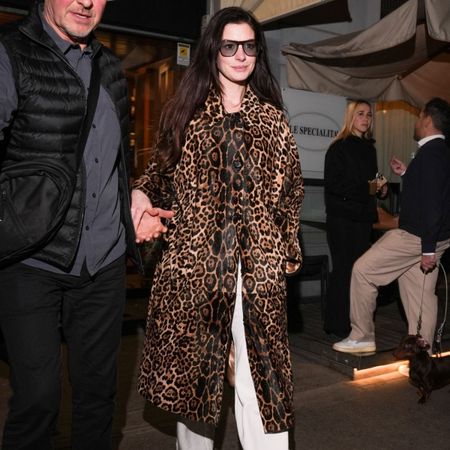 An image of Anne Hathaway wearing a leopard print coat with white jeans and clogs whilst out in Milan.