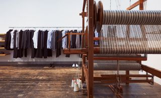 Wooden loom against a background of a clothes rail containing jackets, trousers and shirts