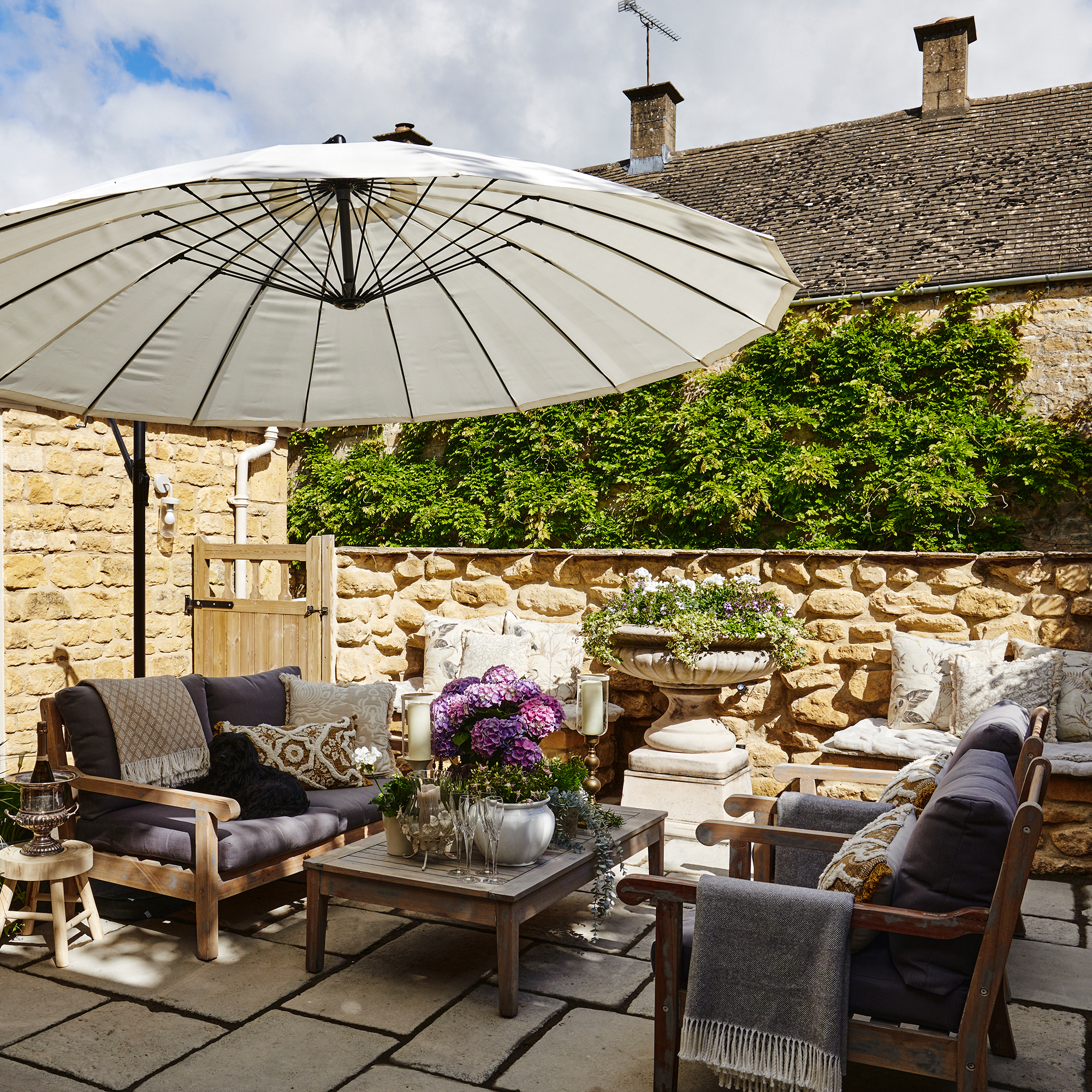 courtyard garden with cotswold stone walls, large parasol and garden sofas