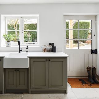 utility room with white wall, back door, grey cabinets with sink