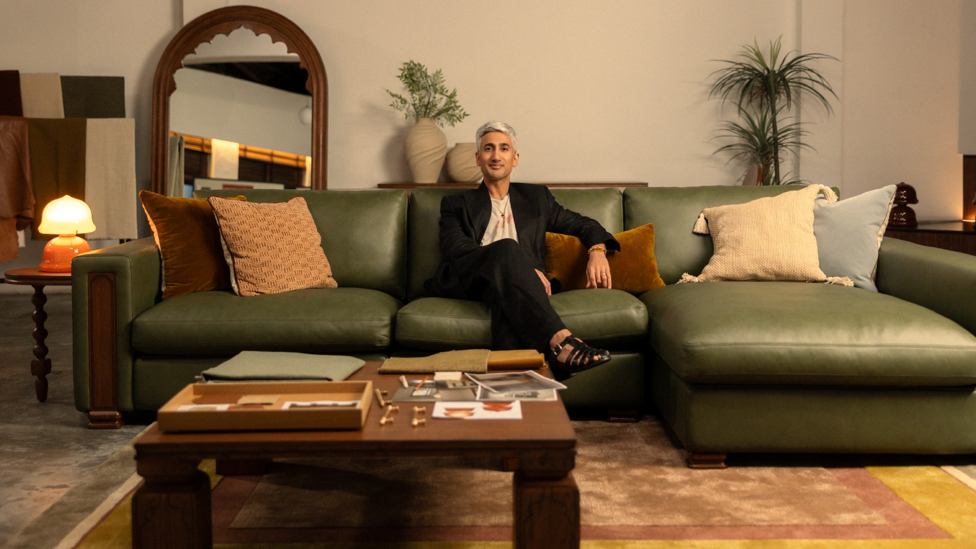 Tan France sitting on the modular chaise sofa from his Castlery collection in green leather with a square tea table in front of him 
