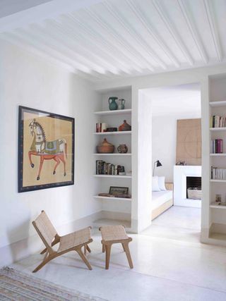 A hotel room sitting area with a wooden chair, a wooden table, a white sofa, two bookshelves, a fireplace and wall paintings.