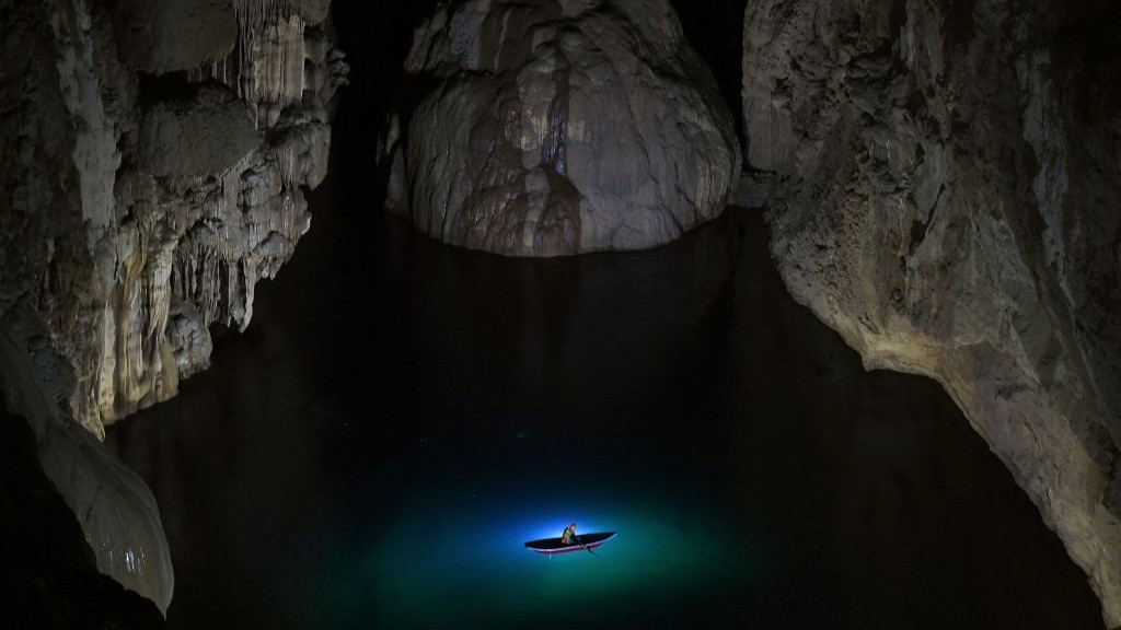 View of the inside of Son Doong cave. There is a lake at the bottom of the cavern and a boat with blue lights.