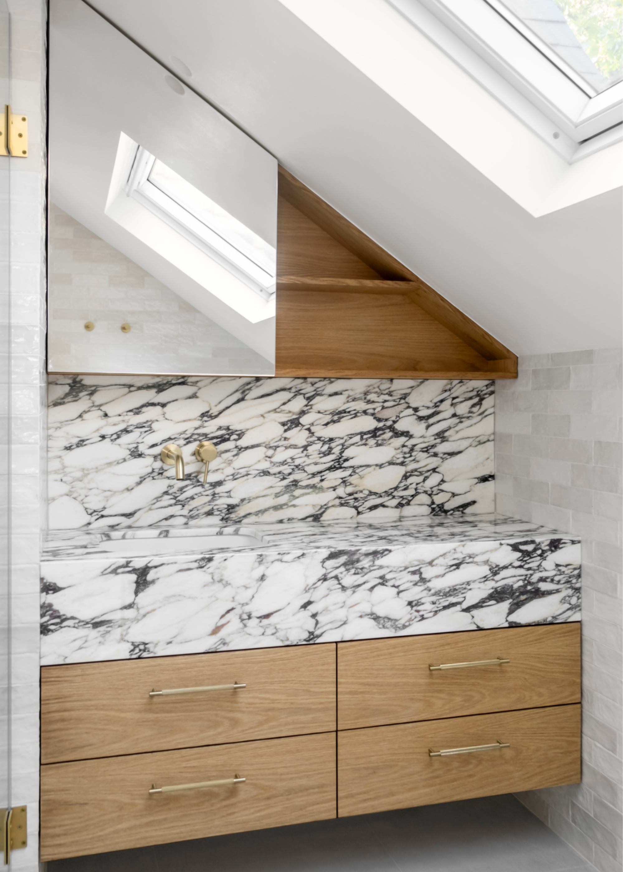 an attice bathroom with a white marble counter with dark veining and wooden drawers